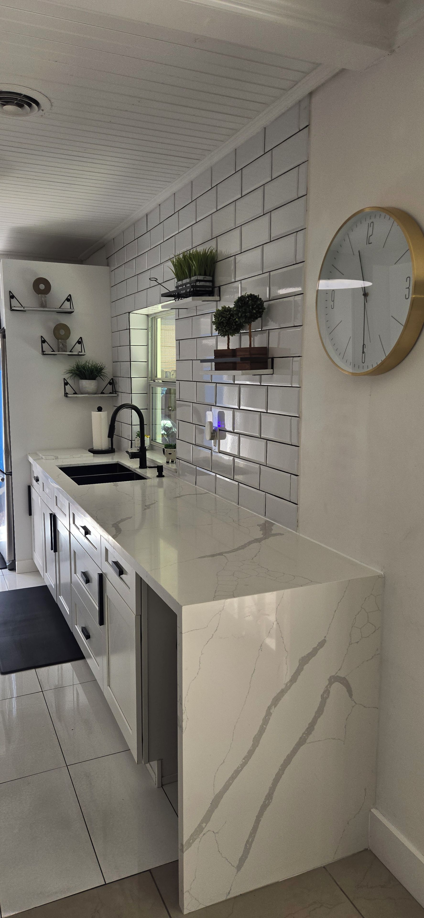 A modern kitchen with a white marble island, a built-in sink, and a large wall-mounted clock.