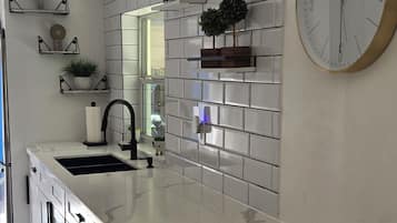 A modern kitchen with a white marble island, a built-in sink, and a large wall-mounted clock.
