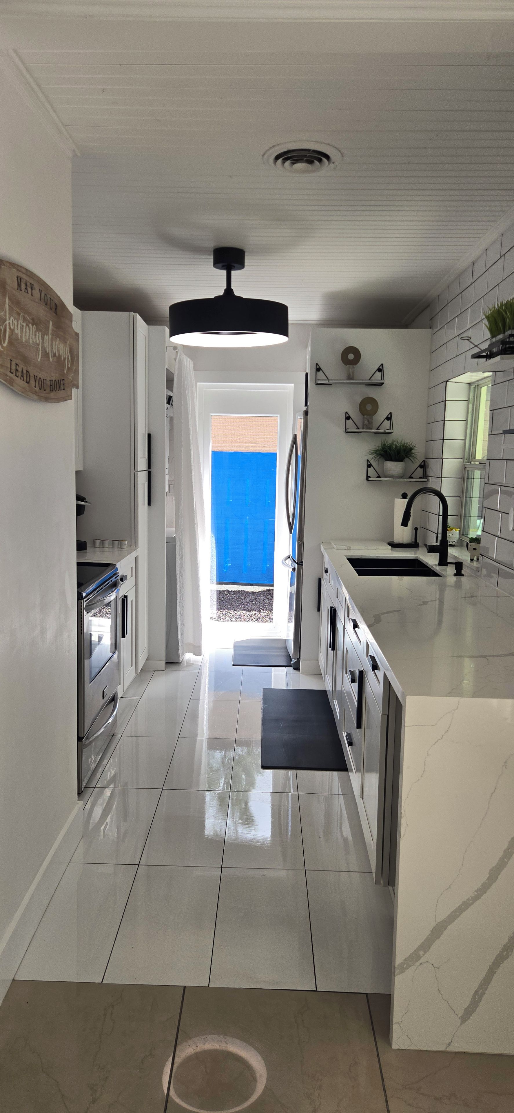 A modern kitchen with a central island, a built-in oven, and a view through an open door to a blue outdoor area.