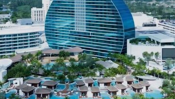 A modern building with a guitar-shaped design, surrounded by a pool and resort-style accommodations.