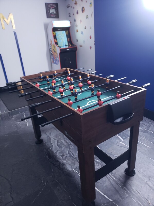 A foosball table in a room with a blue wall and a small arcade machine in the background.