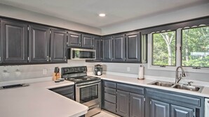 A modern kitchen with dark cabinets, stainless steel appliances, and a large window providing natural light. - Table Rock Lake Hideaway w/ Deck: Bring Your Boat! (Golden)