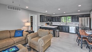 A modern kitchen with dark cabinetry, a central island, and a dining area with wooden chairs and a table. - Table Rock Lake Hideaway w/ Deck: Bring Your Boat! (Golden)