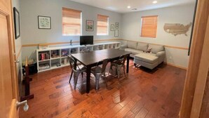 Une pièce avec un plancher en bois, une table à manger avec des chaises, un canapé et un téléviseur posé sur un meuble.
