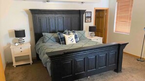 Une chambre à coucher avec un lit en bois foncé, deux tables de chevet avec des lampes, une porte et une fenêtre avec des stores.