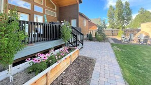 Une maison moderne dotée d’une terrasse en bois, d’un porche couvert et d’un chemin en briques menant à la porte d’entrée.