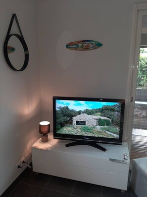A flat-screen TV on a white cabinet, a wall-mounted mirror, and a small table with a lamp.