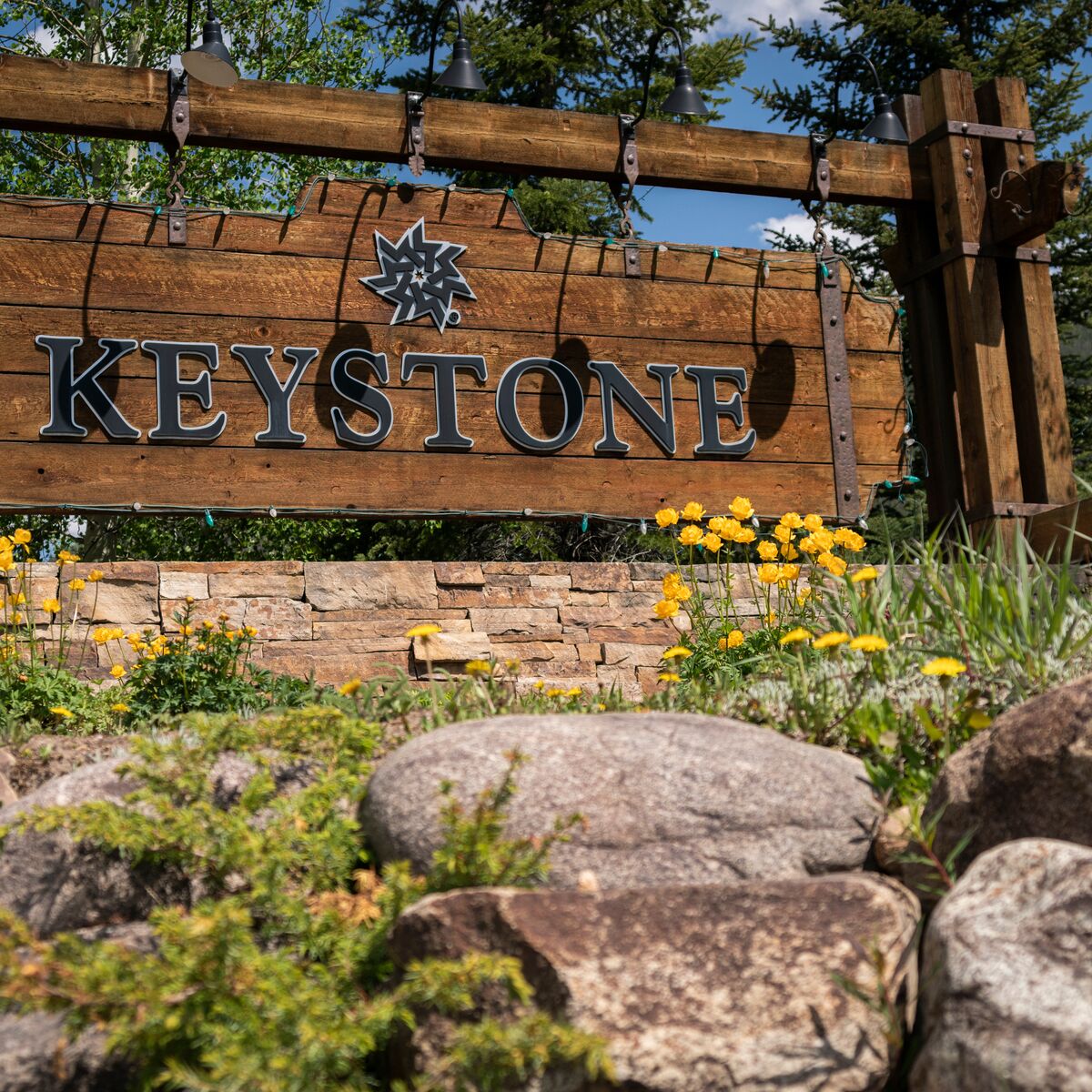 Un panneau en bois portant le mot « KEYSTONE » et un symbole d’étoile, entouré de rochers et de fleurs jaunes.