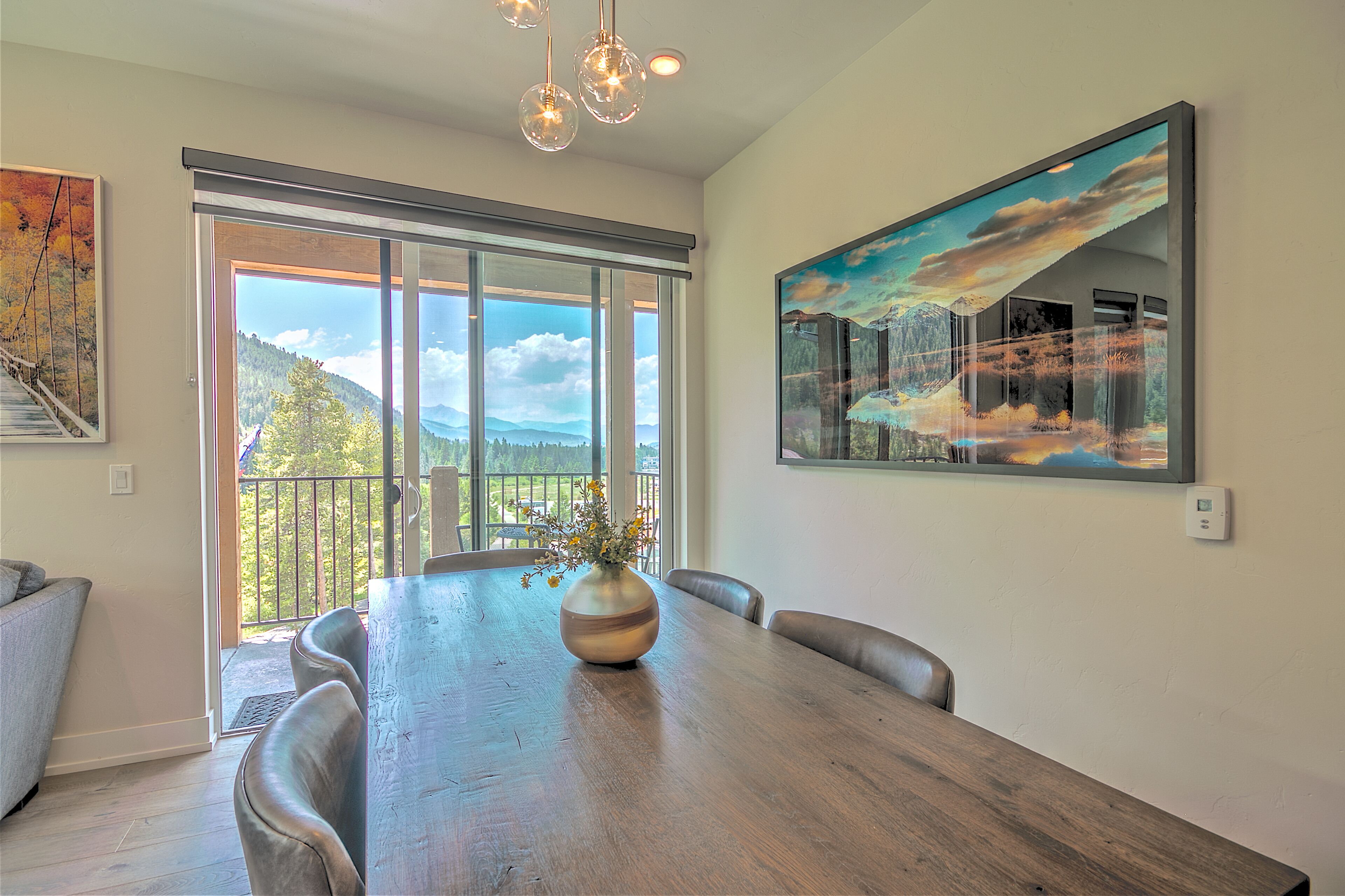 A dining area with a large wooden table, a vase with flowers, and a painting of a mountain landscape.