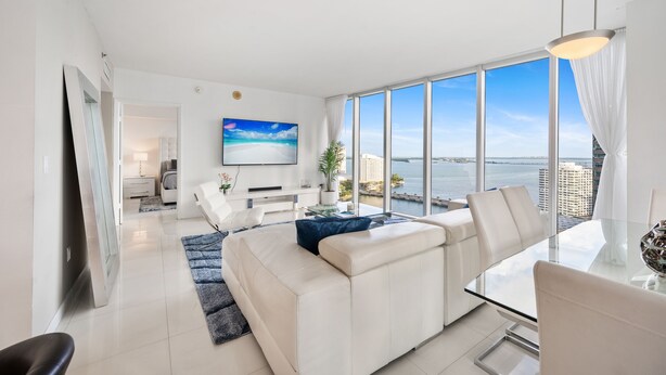 A modern living room with a large window, a sofa, a glass table, and a TV. - ICON BRICKELL • CORNER TWO BEDROOM• OCEAN VIEW (Miami)