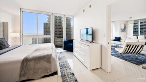 A modern hotel room with a large bed, a TV, a desk, and a view of the cityscape. - ICON BRICKELL • CORNER TWO BEDROOM• OCEAN VIEW (Miami)