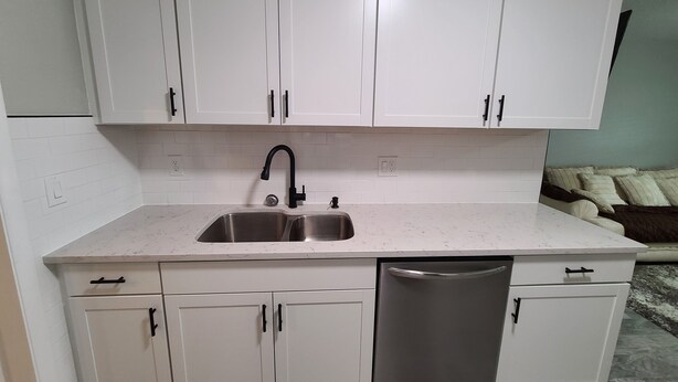 A kitchen with white cabinets, a stainless steel sink, and a dishwasher. - Cheerful Home by the Springs  (North Port)