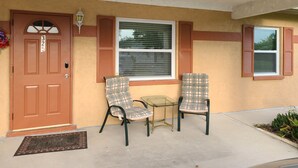 A house entrance with a brown door, two plaid chairs, a small glass table, and a window with shutters. - Cheerful Home by the Springs  (North Port)