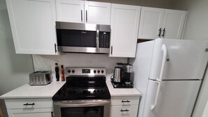 A kitchen with white cabinets, a stainless steel microwave, a stove, a coffee maker, and a white refrigerator. - Cheerful Home by the Springs  (North Port)