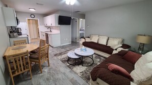 A compact living space with a dining area, a sofa, a coffee table, and a kitchen in the background. - Cheerful Home by the Springs  (North Port)