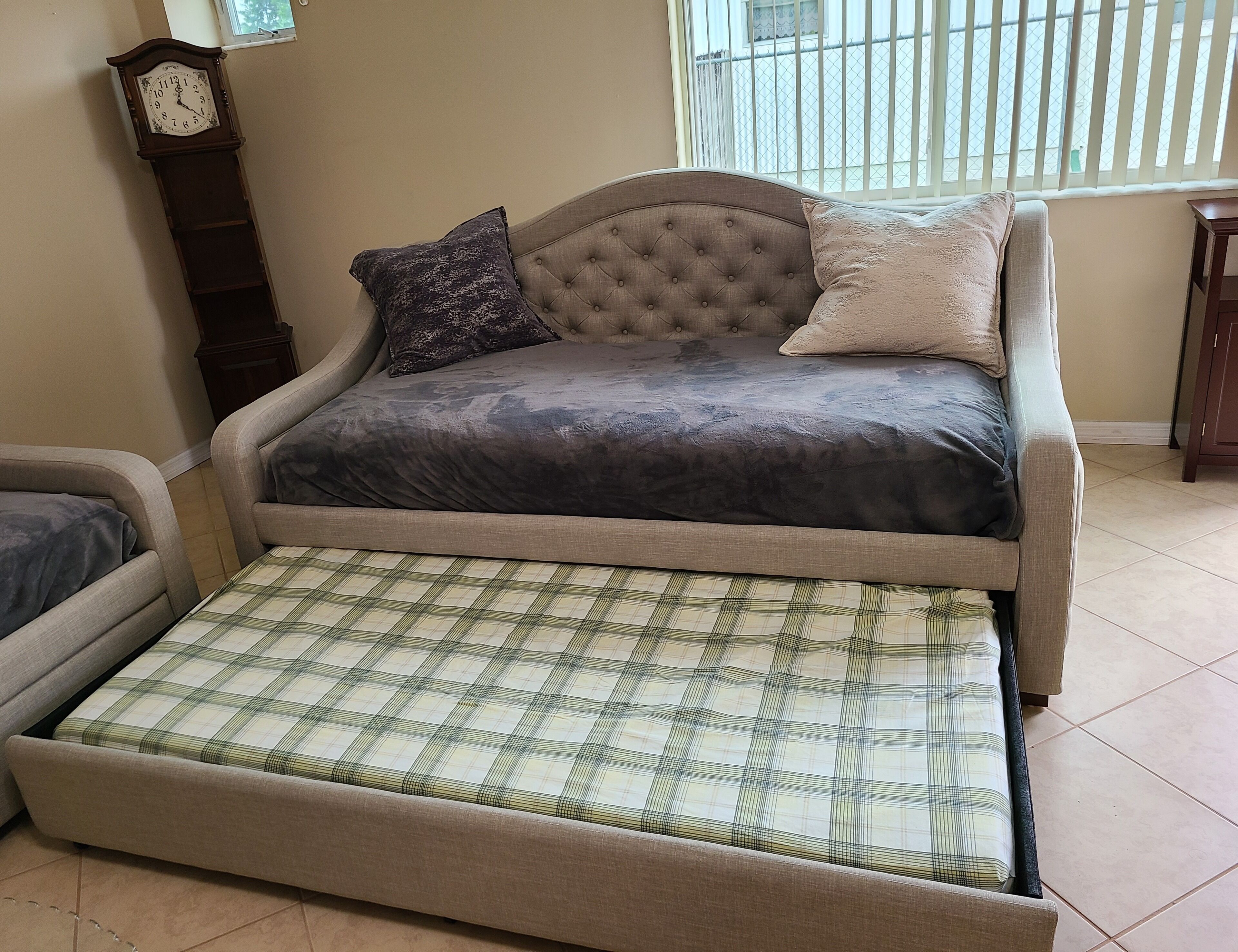 A sofa bed with a plaid cover, a tufted headboard, and two pillows.