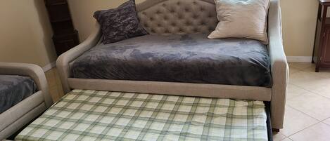A sofa bed with a plaid cover, a tufted headboard, and two pillows.