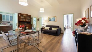 Ein stilvoller Wohnbereich mit einem Glastisch, einem dunklen Sofa und einer Küchenzeile mit Holzschränken.