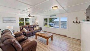 A living room with a brown leather sofa, a wooden coffee table, and a ceiling fan. - Mille lacs Lake Beach House-Water Front-SAND-Fish (Wahkon)
