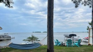 A hammock tied to a tree, outdoor chairs, and a table by a lake with a dock in the background. - Mille lacs Lake Beach House-Water Front-SAND-Fish (Wahkon)