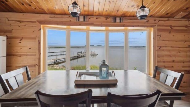A wooden cabin with a dining table and chairs, large windows with a view of a dock and water. - Mille lacs Lake Beach House-Water Front-SAND-Fish (Wahkon)