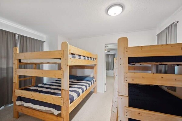 Una habitación con dos literas, una lámpara en el techo y una puerta que da a otra estancia.