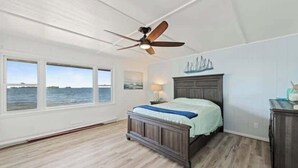 A bedroom with a bed, a ceiling fan, a window with a view of the water, and a wall-mounted ship decoration. - Mille lacs Lake Beach House-Water Front-SAND-Fish (Wahkon)