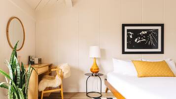 Une chambre d’hôtel avec un lit, un bureau, une chaise, une lampe, un tableau encadré et une plante en pot.