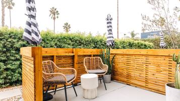 A wooden outdoor seating area with wicker chairs and a small round table, surrounded by a wooden fence and greenery.