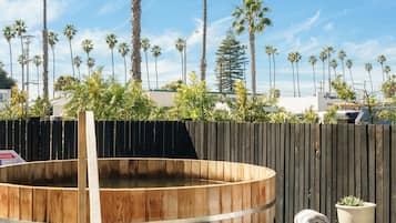 Un jacuzzi de madera con escalera, rodeado de una valla de madera, y palmeras con un cielo azul despejado al fondo.