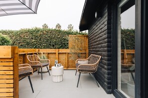 Een terras buiten met rieten stoelen, een ronde tafel en een houten omheining.