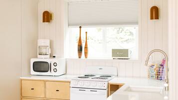 Una cocina con estufa blanca, microondas, armarios de madera y una ventana con persianas.