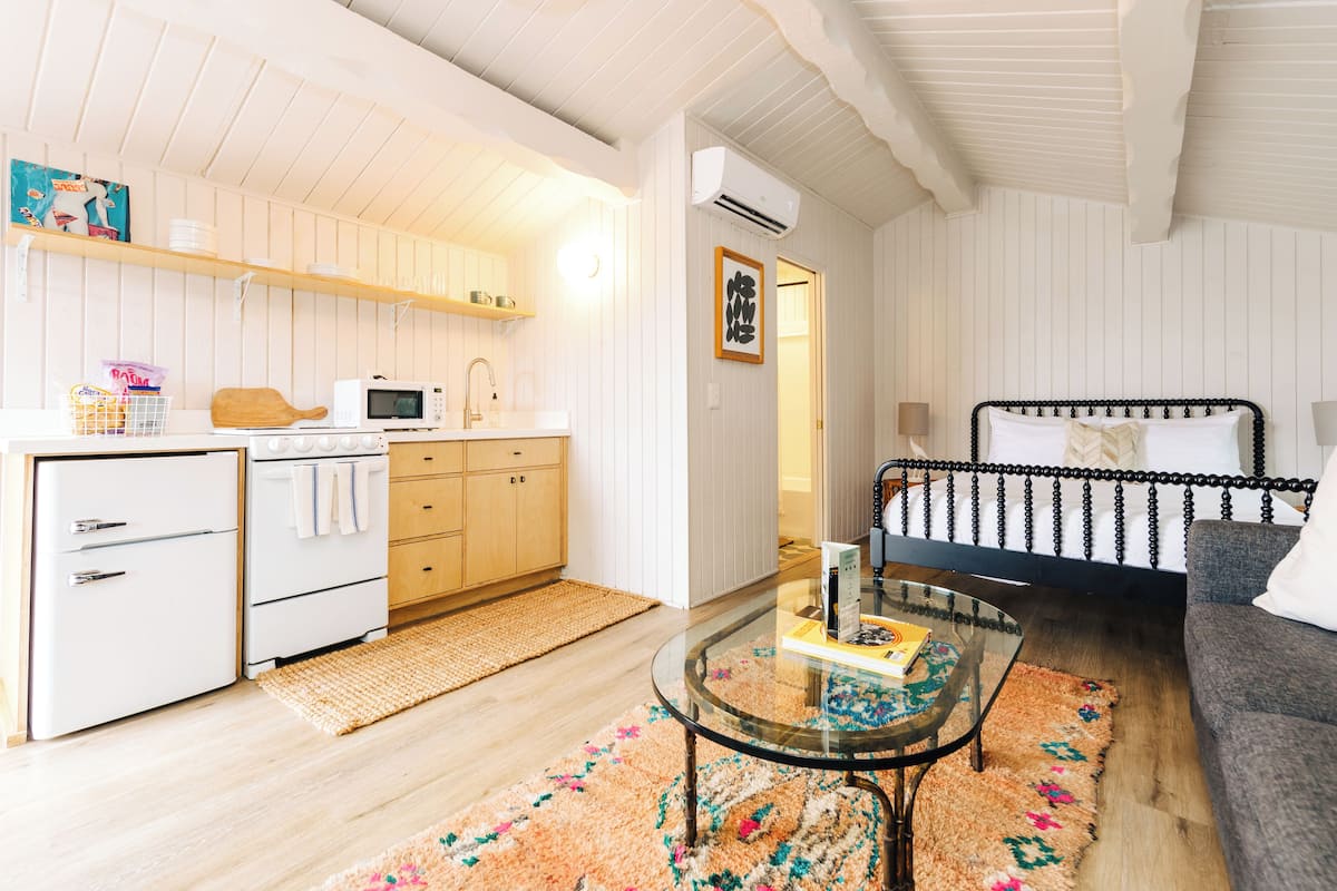 A compact living space with a kitchenette, a bed, a glass coffee table, and a patterned rug.