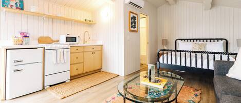 A compact living space with a kitchenette, a bed, a glass coffee table, and a patterned rug.