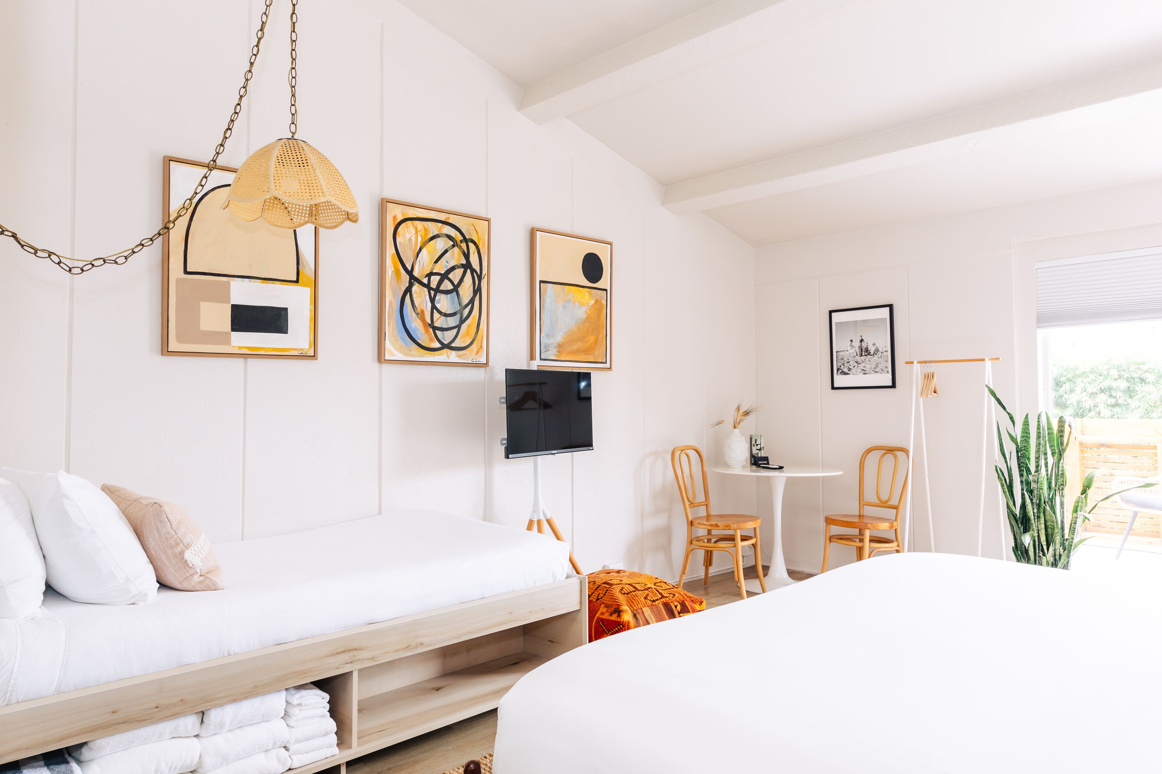 Un dormitorio moderno con cama, escritorio y silla. Hay pinturas abstractas en la pared y un televisor.