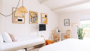 Un dormitorio moderno con cama, escritorio y silla. Hay pinturas abstractas en la pared y un televisor.