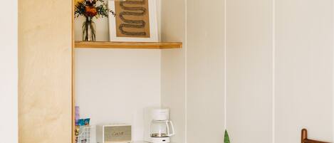 Un dormitorio con cama, armario de madera, escritorio con cafetera y una planta.