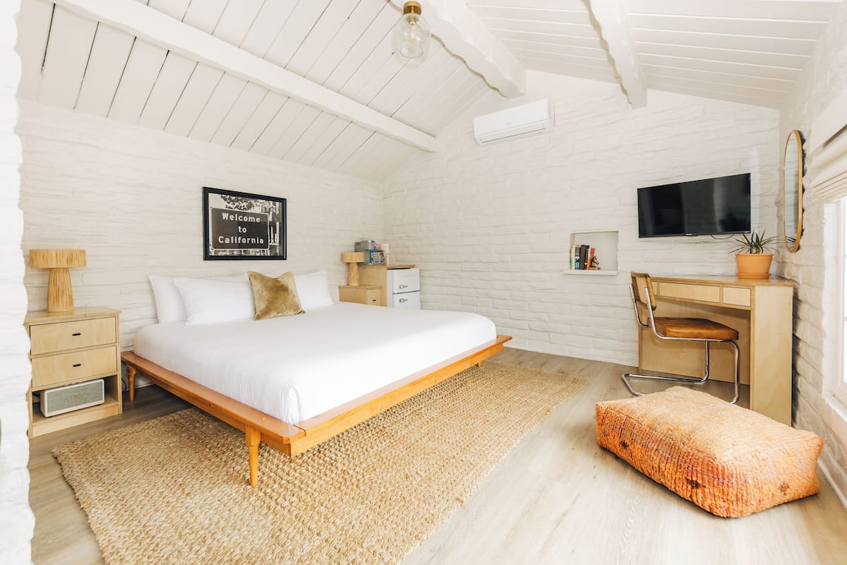 A bedroom with a bed, bedside tables, a desk, a chair, a TV, and a window.