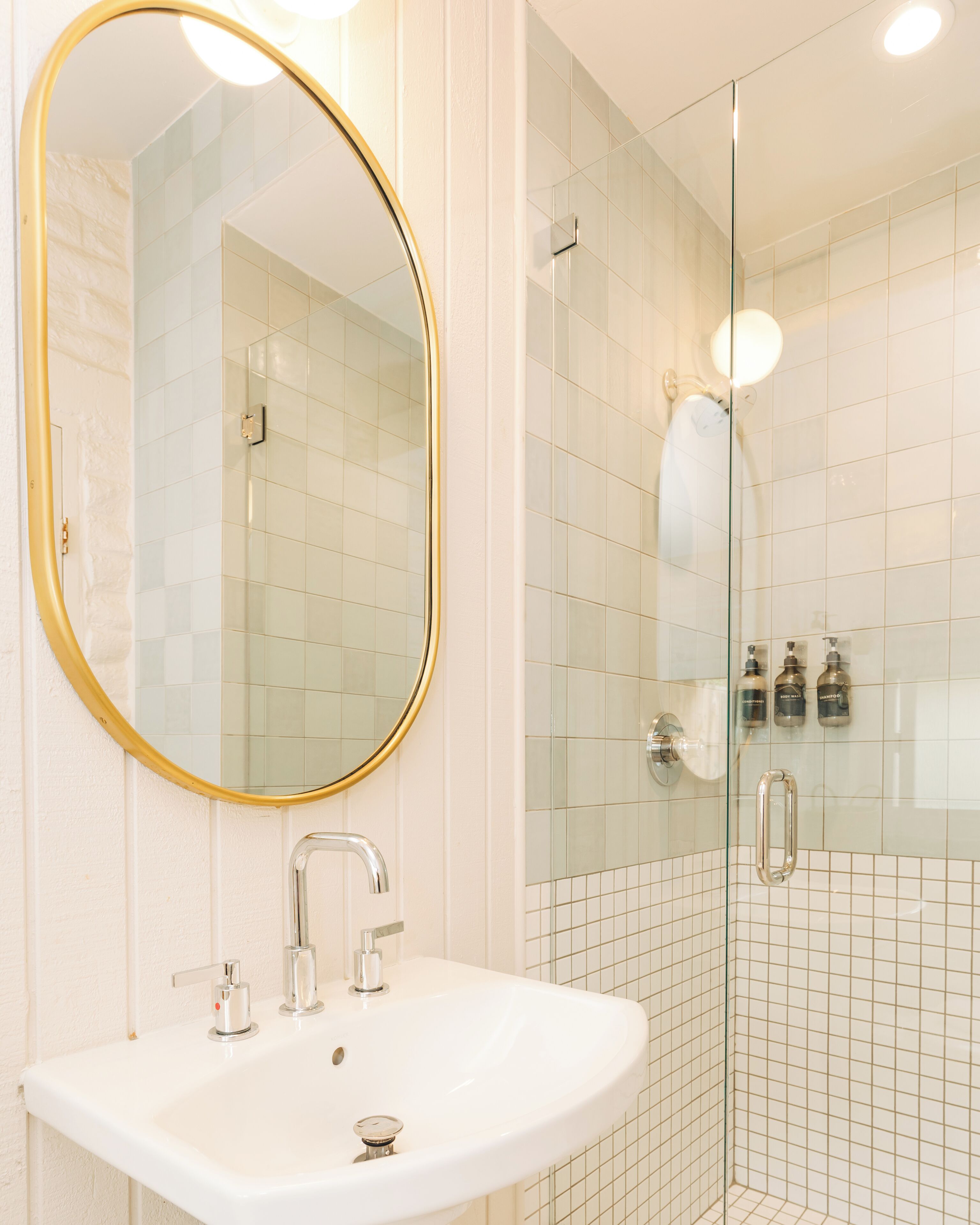 Un bany amb un lavabo blanc, un mirall rodó amb marc daurat i una cabina de dutxa de vidre.
