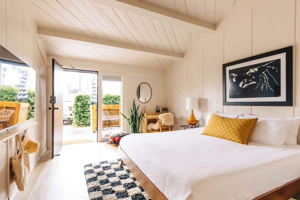 A bedroom with a large bed, a desk, a chair, and a view of the outdoors.