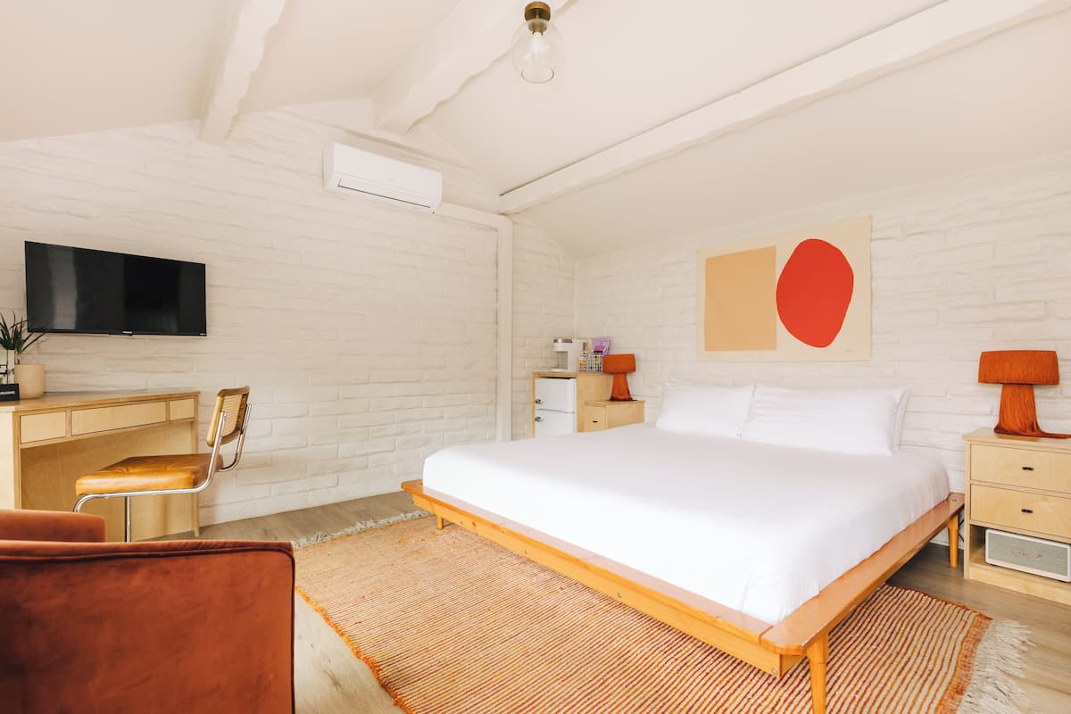 A bedroom with a bed, a desk, a chair, a TV, and a wall-mounted air conditioner.