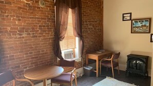 A cozy room with a brick wall, a round wooden table, two chairs, a radiator, a radiator cover, a vintage radio, and a framed picture on the wall. - Historic Commercial Hotel(Est.1868) "Dam Room" (Osceola)