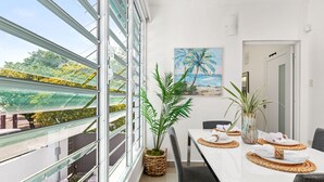 Ein Essbereich mit großem Fenster, einem Palmen-Gemälde und Blick auf Grünfläche.