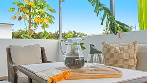 Eine Terrasse mit Korbstuhl, Tisch, Wasserkaraffe, Gläsern und einem Holzboden.