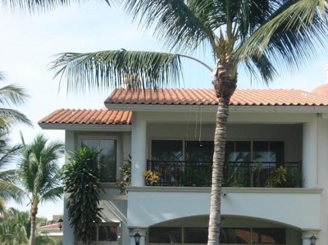 A two-story building with a red-tiled roof, large windows, and a balcony with plants.