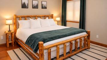 A wooden-framed bed with white bedding and a green throw, flanked by two bedside lamps, in a room with a striped rug and framed pictures on the wall.