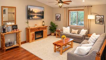 A cozy living room with a fireplace, a sofa set, a coffee table, and a large window with curtains.