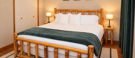 A bed with a wooden frame, white bedding, and a green throw. There are two bedside tables with lamps.