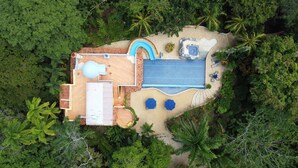 Vue aérienne d’un complexe hôtelier doté d’une piscine, d’un jacuzzi et d’un espace salon abrité, le tout entouré d’une végétation luxuriante.