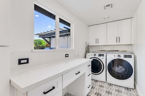 A compact laundry room with two washing machines, a window, and a white countertop. - Resort-Style Home w/ Private Heated Pool-Old Town (Scottsdale)